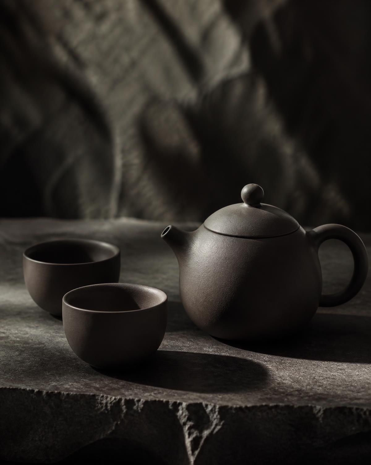 Unglazed clay teapot and cups on a stone surface